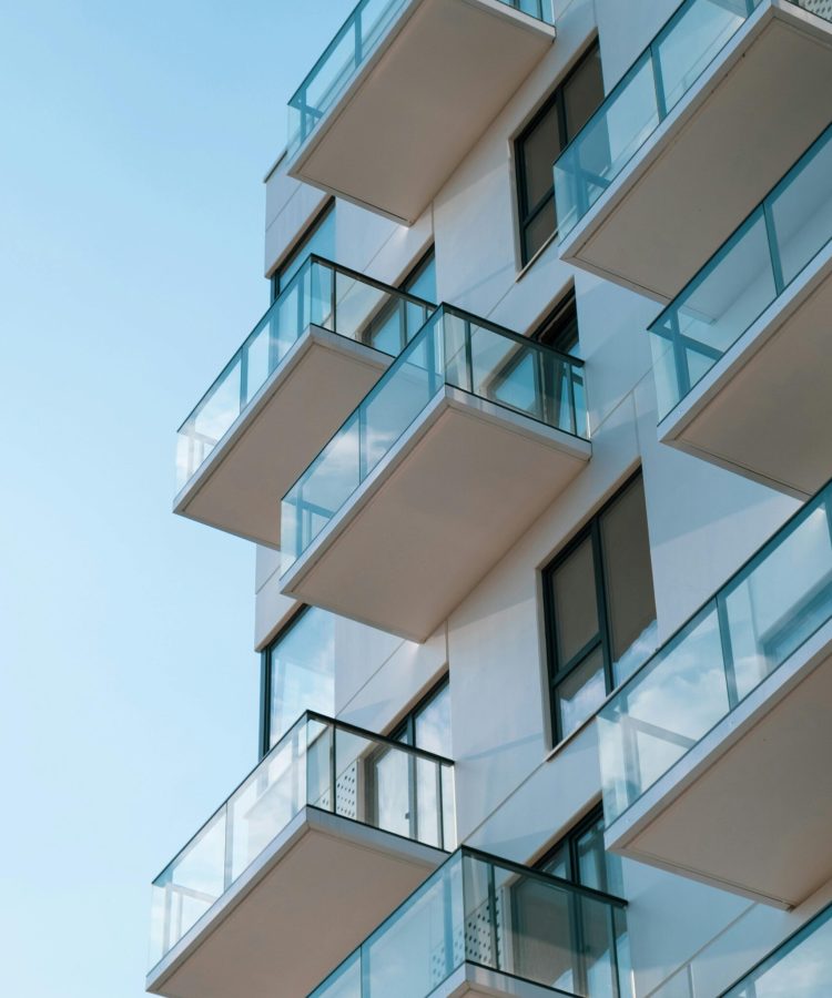 Stylish residential building featuring glass balconies against a clear blue sky.